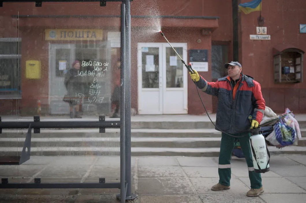 Сотрудник ЖКХ в Киеве проводит санобработку автобусной остановки. Фото: EPA