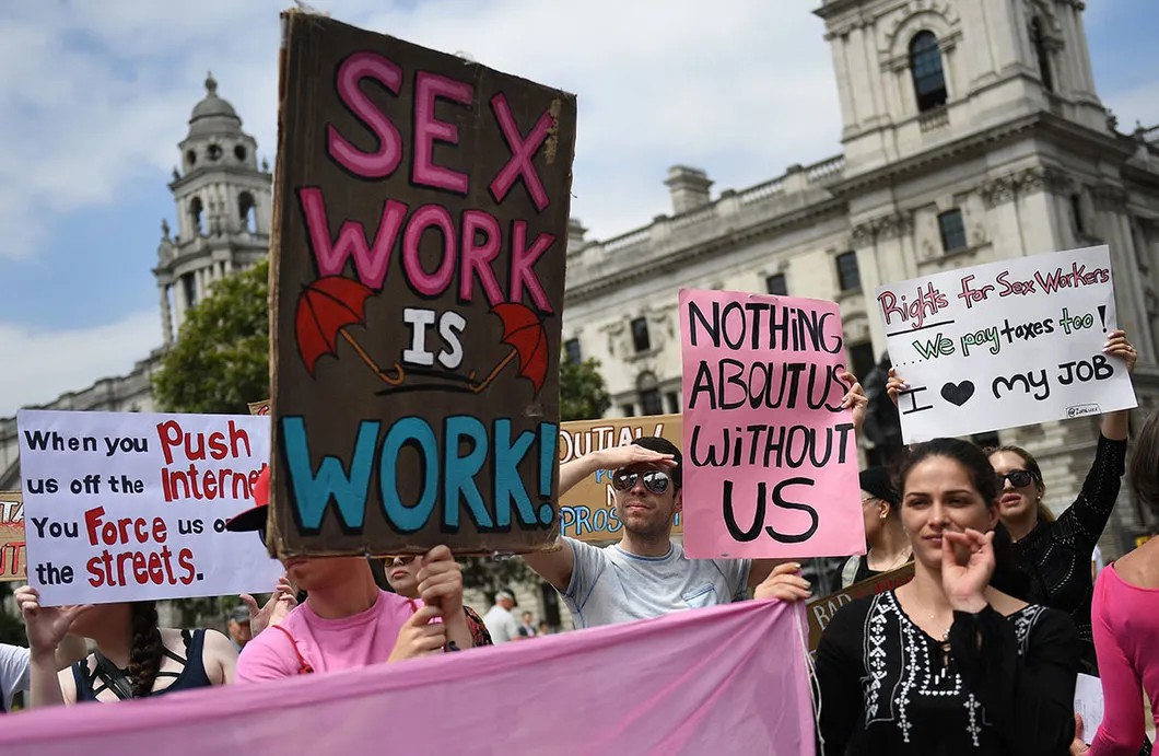 Пикет секс-работников у британского парламента. Надписи на плакатах: «Секс-работа — это работа», «Ничего, что касается нас, без нашего участия», «Мы тоже платим налоги! Я люблю свою работу». Лондон, 2018 год. Фото: Andy Rain / EPA