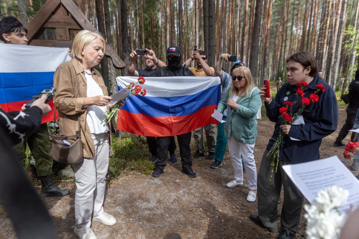 Эмилия Слабунова, член Федерального политического комитета «Яблока» и руководитель фракции партии в Заксобрании Карелии, читает имена жертв репрессий. Ее окружили посетители мемориала и провокаторы с российскими флагами. Фото: Алексей Душутин / «Новая газета»