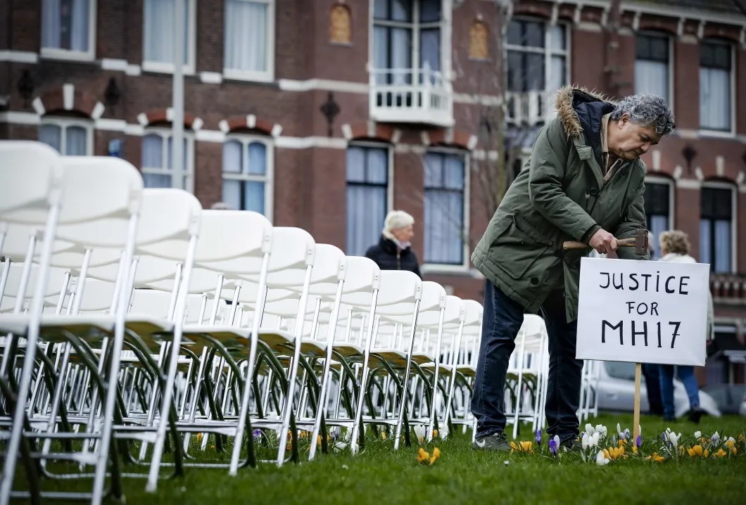На газоне перед зданием выставили баннер «Человечность превыше политики» и 298 белых стульев, каждый их которых символизирует одну унесенную катастрофой жизнь. Фото: EPA