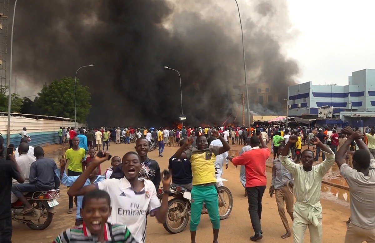 Демонстрация в поддержку мятежников, отстранивших от власти президента Нигера Мохамеда Базума, проходит на фоне горящей штаб-квартиры правящей партии в Ниамее. Фото: AP / TASS