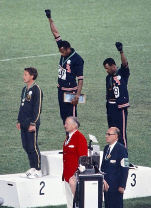 Золотой призер Томми Смит (в центре) и бронзовый призер Джон Карлос (справа) демонстрируют поднятый кулак на пьедестале почета после забега на 200 метров на летних Олимпийских играх 1968 года. Фото: Википедия