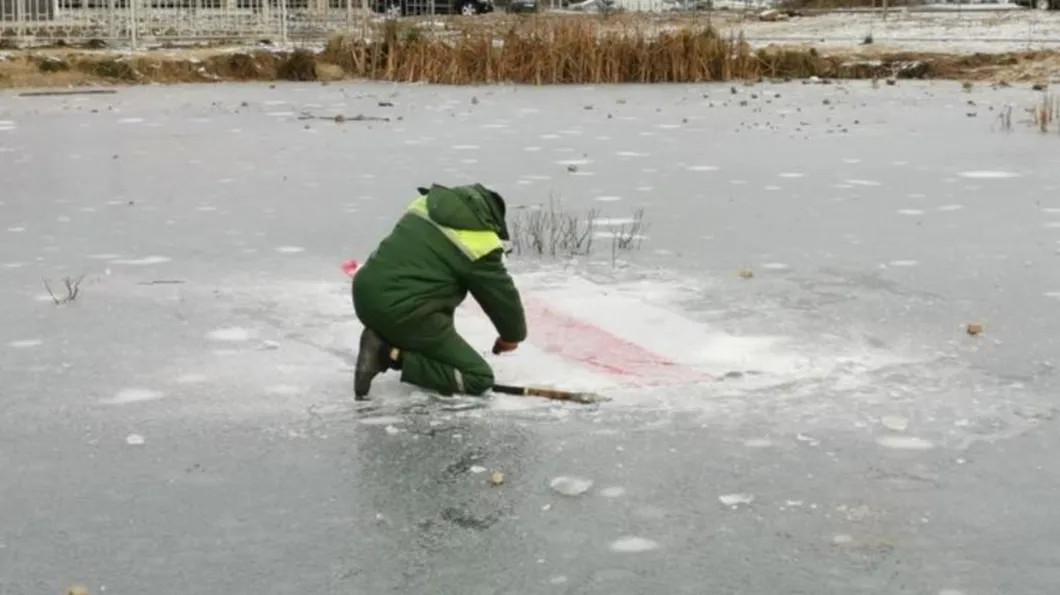 Сотрудник коммунальной службы вырубает вмерзший в лед бело-красно-белый флаг. Фото: читатель TUT.by