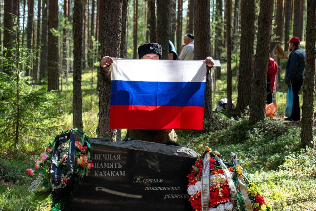 Представитель казачьей общины Карелии с российским флагом у памятника казакам, погибшим во время политических репрессий. Фото: Алексей Душутин / «Новая газета»