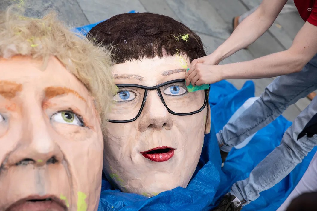Протестующие делают маски Меркель и АКК. Фото: EPA