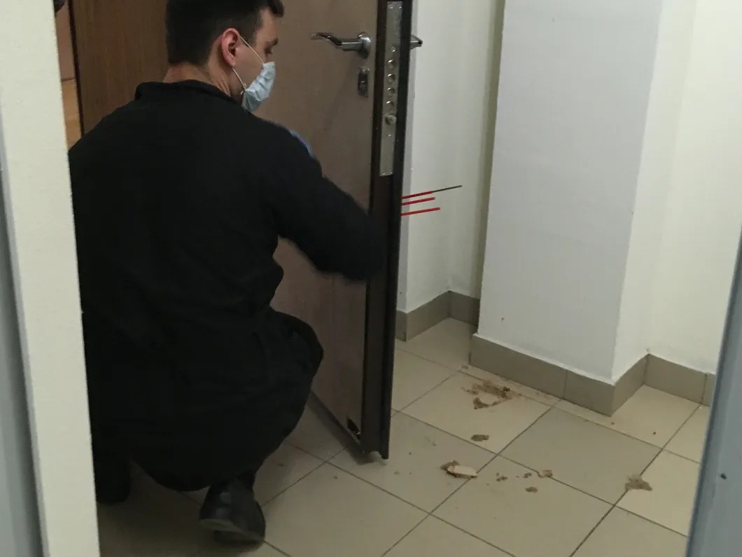 Криминалист изучает пулевые отверстия в двери квартиры Таушанкова. Фото: Изольда Дробина / «Новая газета»