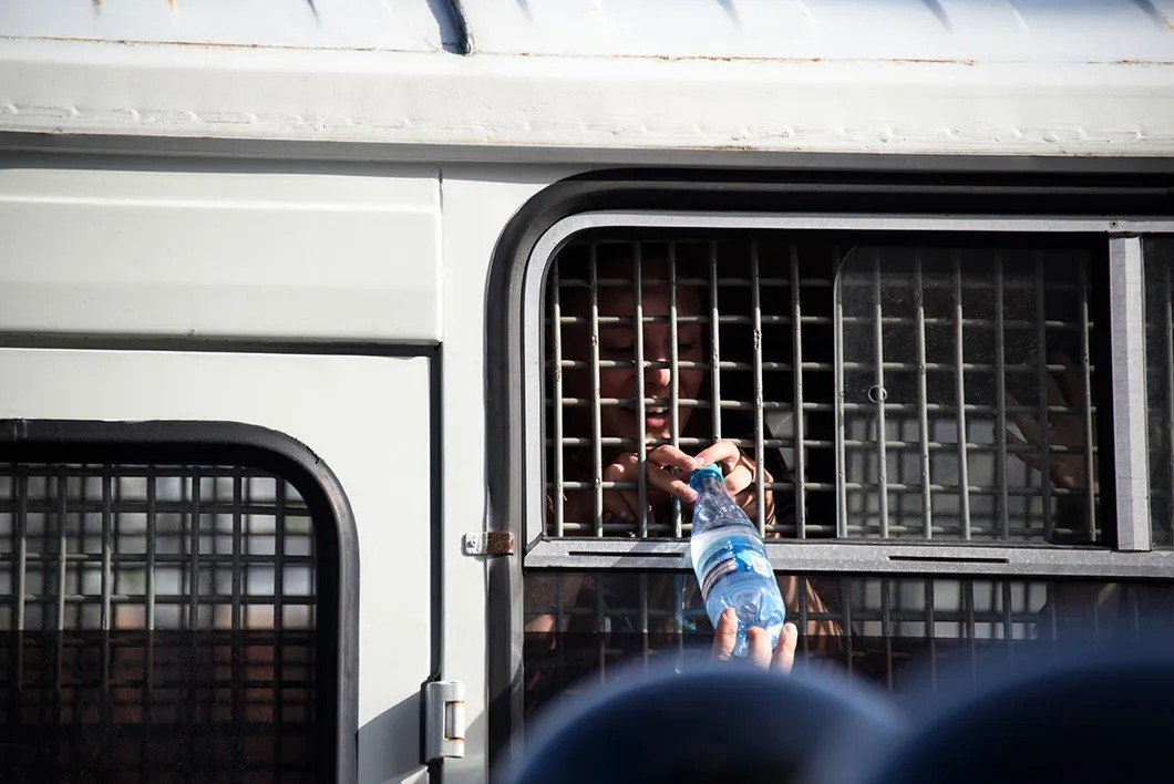 Люди протягивают бутылки воды в автозак задержанным. Фото: Виктория Одиссонова / «Новая газета»