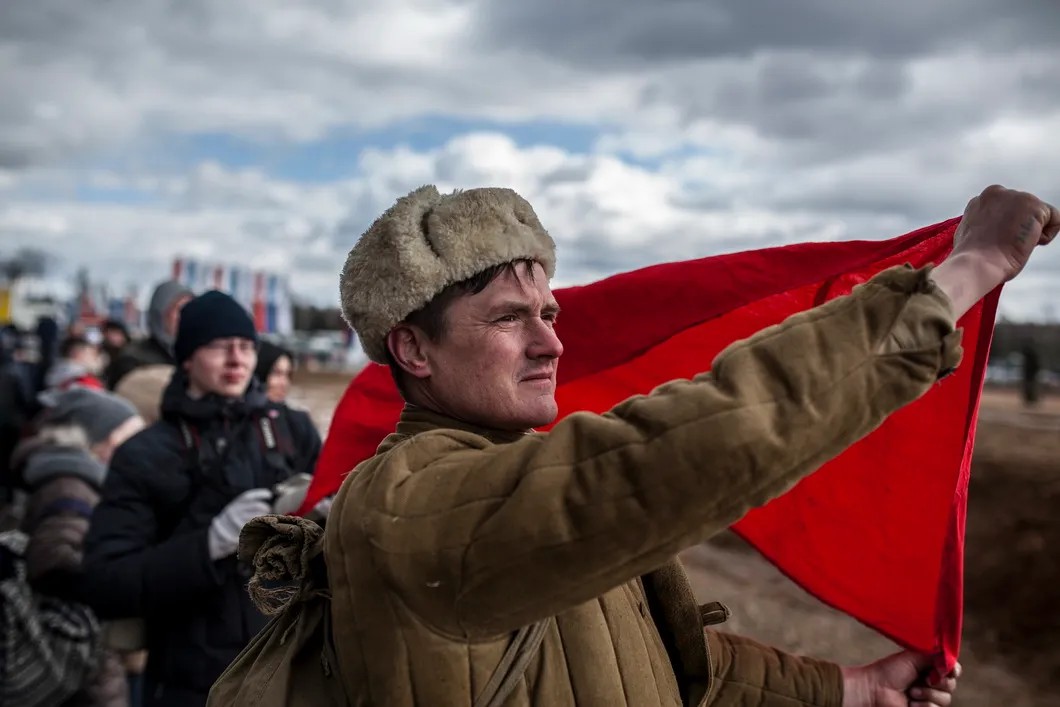 Участник реконструкции разворачивает красное знамя после объявления о взятии Рейхстага. Фото: Влад Докшин / «Новая газета»