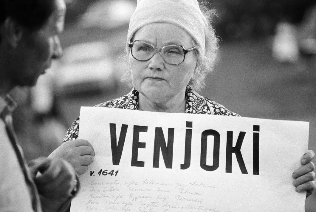 Одна из участниц летнего праздника ингерманландских финнов держит плакат с названием деревни, исчезнувшей после насильственного выселения ее жителей во времена сталинских репрессий, 1989 год. Фото: РИА Новости