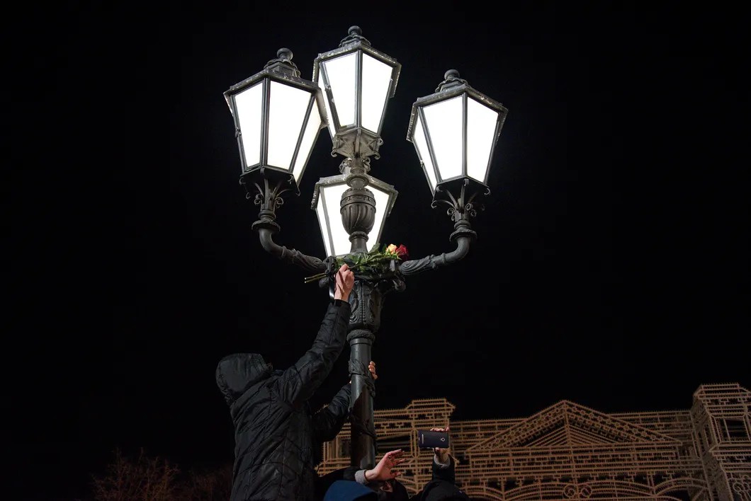 Один из присутствующих кладет цветы на фонарь у памятника Пушкину. Фото: Виктория Одиссонова / «Новая газета»