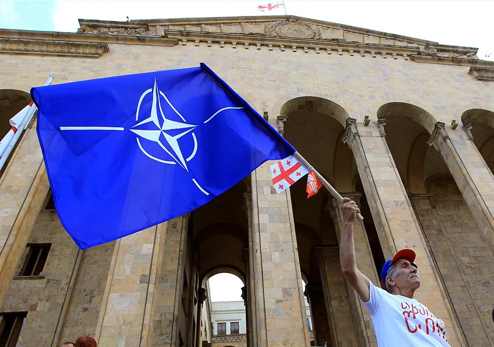 Участник акции протеста держит флаг НАТО у здания парламента Грузии. Фото: ТАСС