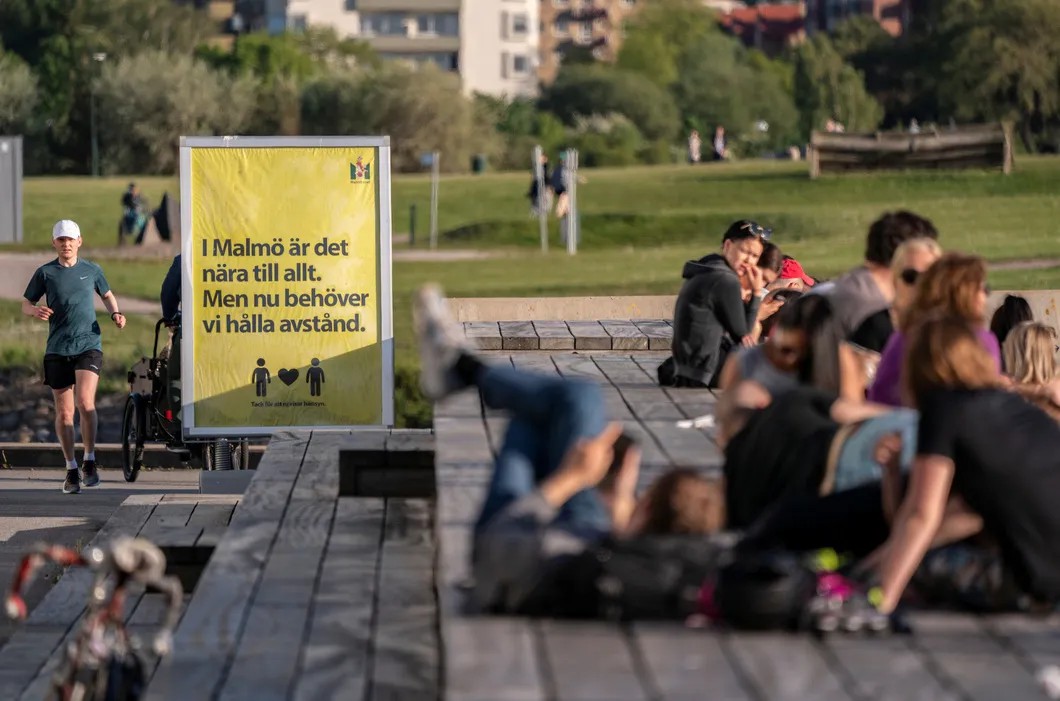 Люди отдыхают на фоне знака, предупреждающего о важности социальной дистанции. Мальмё. Фото: Reuters