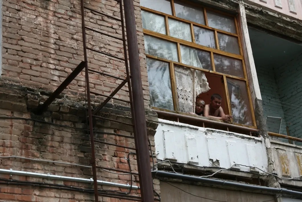 Местные жители выглядывают из окон дома, пострадавшего от зрывной волны. Фото: Михаил Солунин — специально для «Новой»
