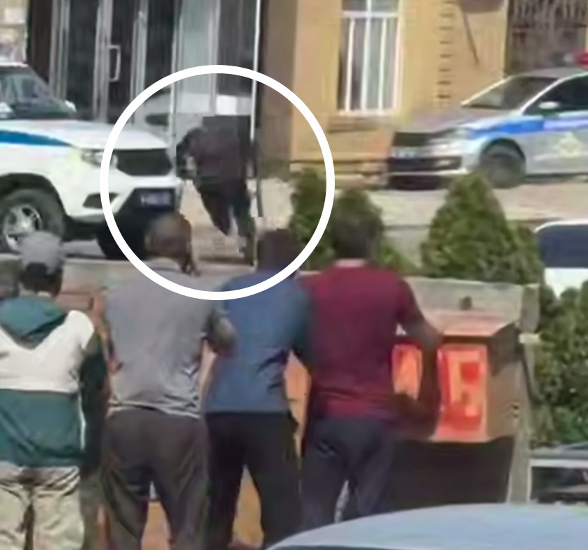 Сотрудник полиции скрывается во время стрельбы на улице. Очевидцы прячутся за металлическим мусорным контейнером. Кадр из видео в соцсетях