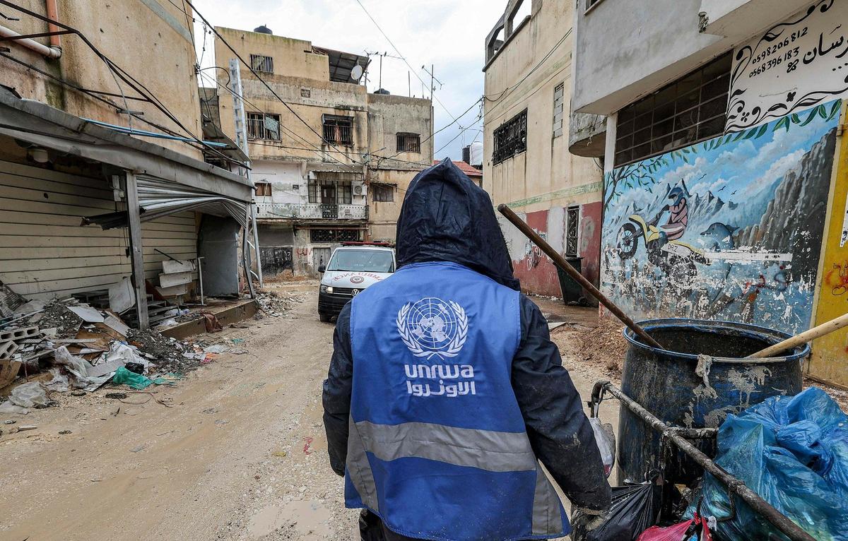 Газа. Мужчина собирает мусор в куртке с логотипом Ближневосточного агентства ООН для помощи палестинским беженцам (БАПОР). Фото: JAAFAR ASHTIYEH / AFP / East News