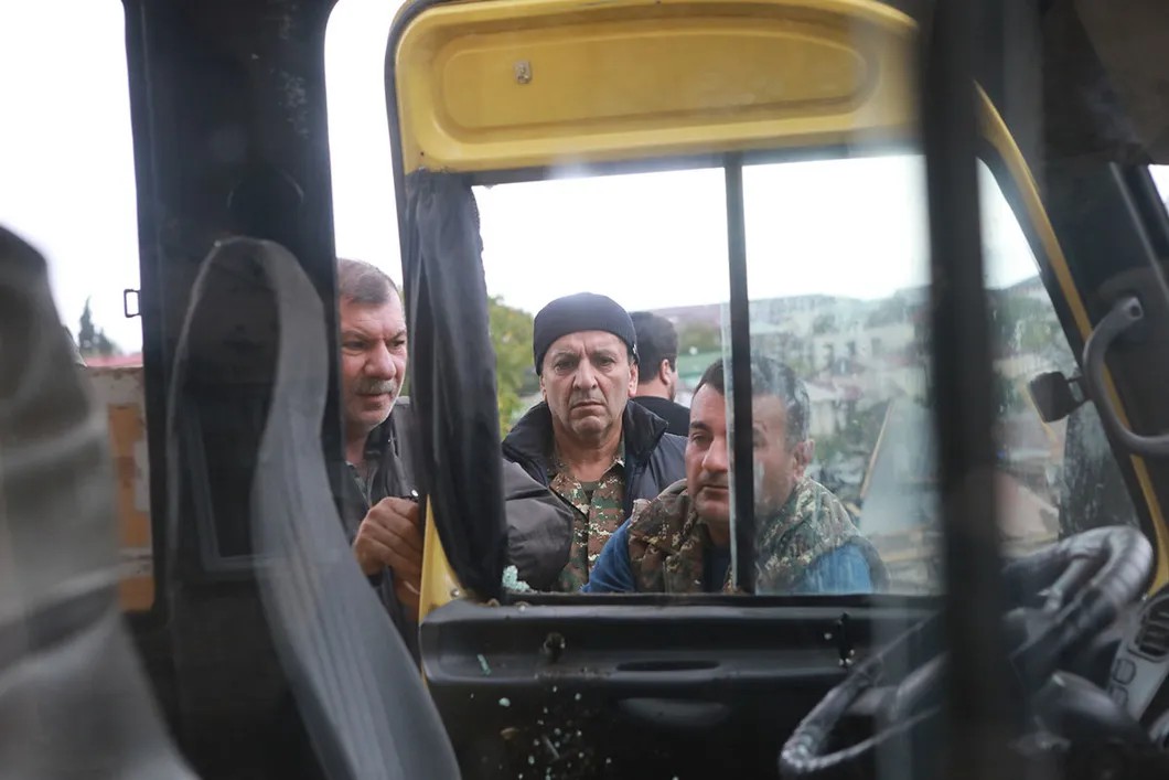 Местные жители пытаются открыть дверь автобуса, пострадавшего от бомбежки. Фото Павел Волков, специально для «Новой»