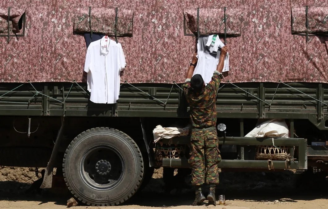 Дежурный военнослужащий снимает развешенные рубашки с военного грузовика на блокпосту в городе, Мьянма. Фото: EPA