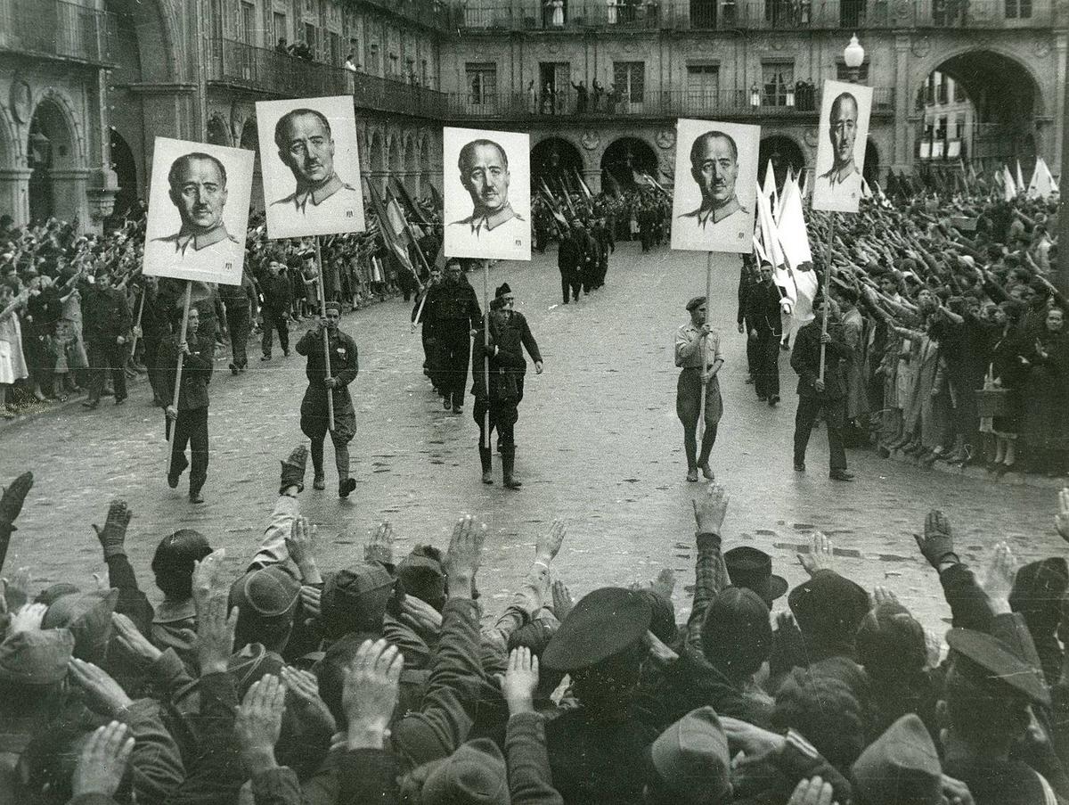 Франкистская демонстрация в Саламанке (1937), участники парада несут знамена с портретом Франко, а население отдает римский салют.